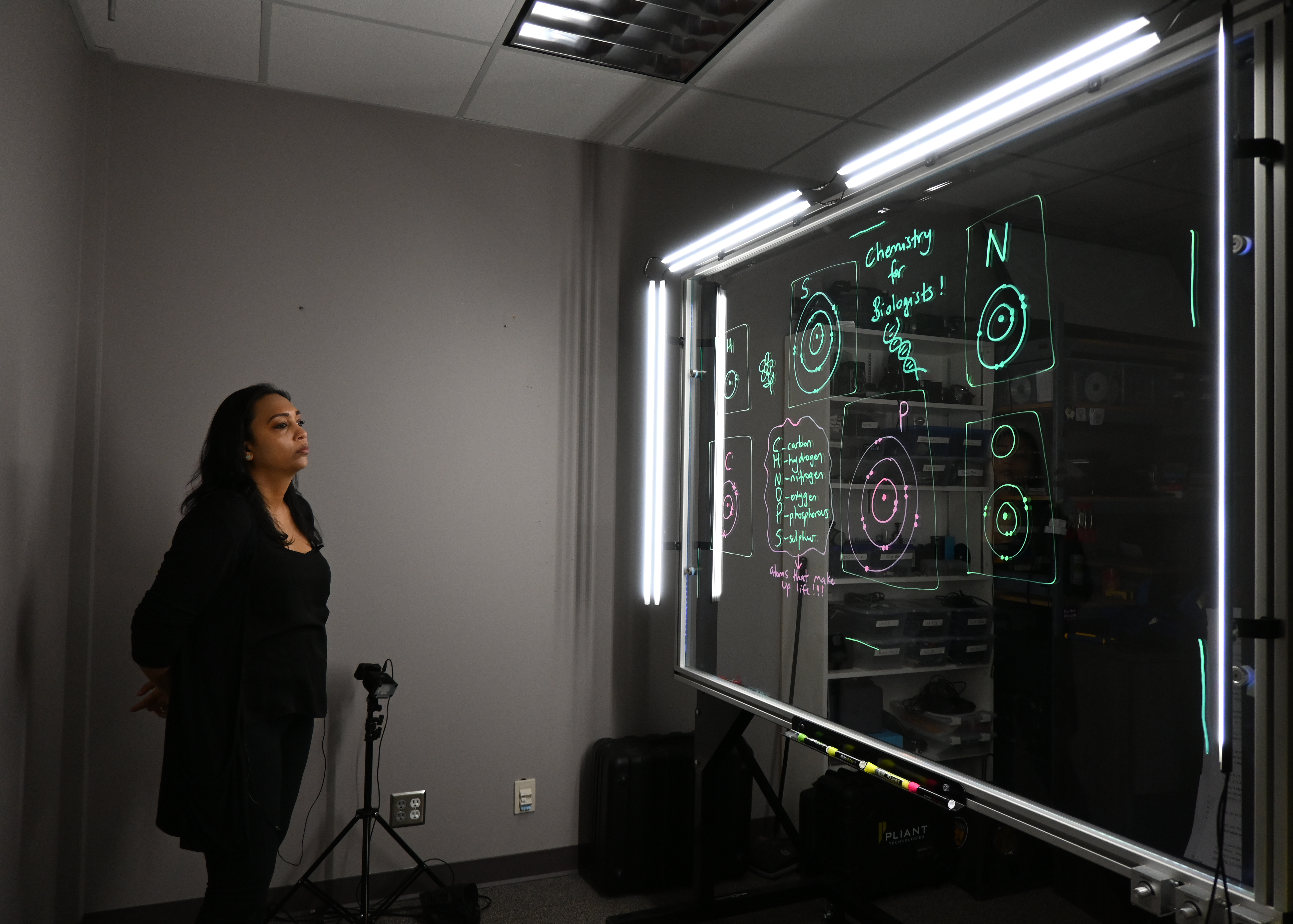 Professor looking at a light board that shows a list of the six elements that make up life along with their Bohr models.