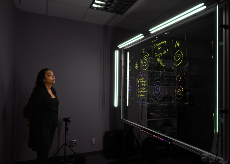 Professor looking at a light board that shows a list of the six elements that make up life along with their Bohr models.