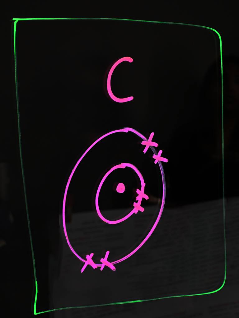 Drawing of a carbon Bohr model on a light board.