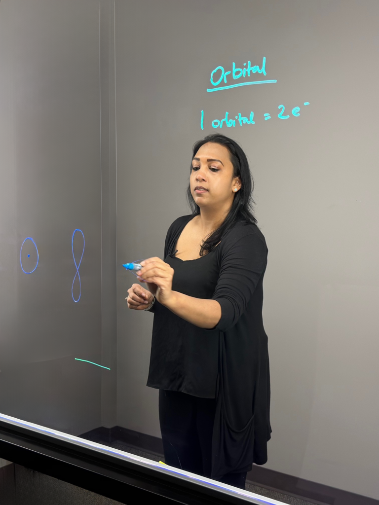 Professor writing on light board to explain orbitals in the Bohr model.