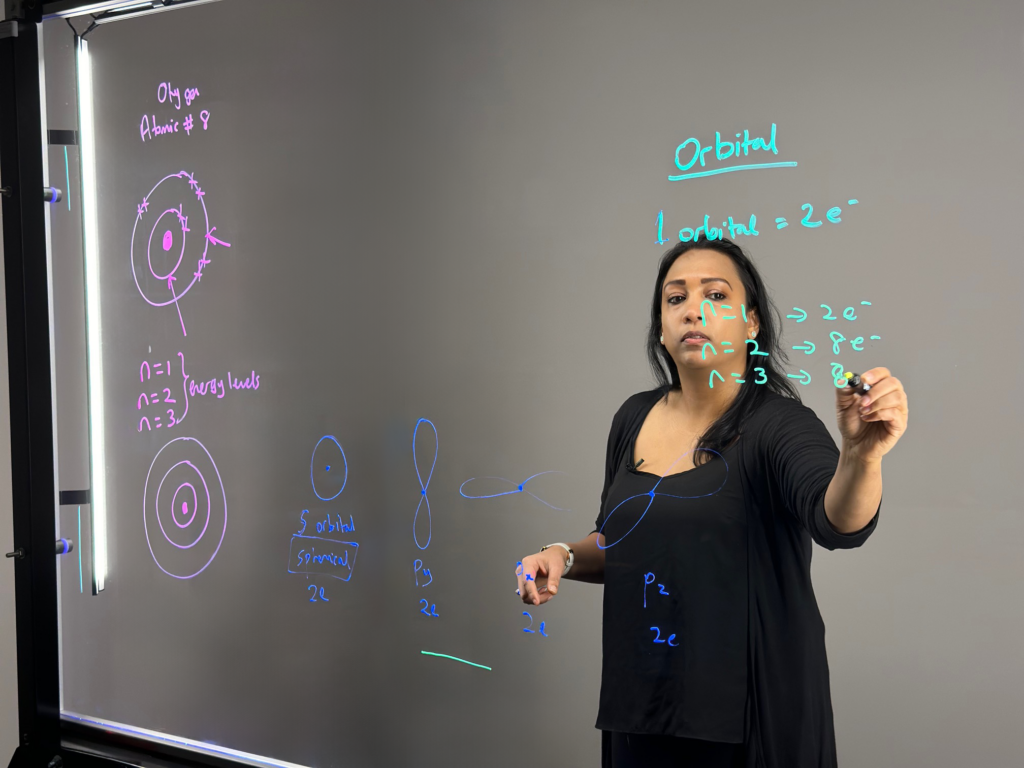 Professor writing on light board to explain orbitals in the Bohr model.